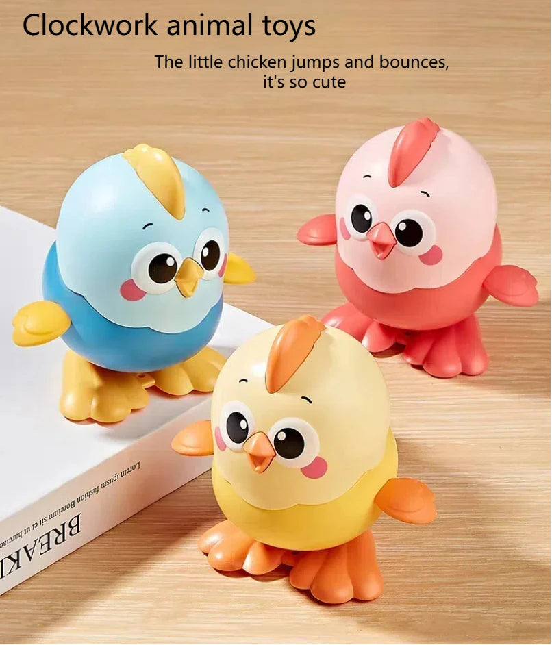 Three colorful clockwork animal toys of chicks in blue, pink, and yellow sitting on a wooden surface.