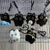 A collection of cute plush black cat keychain charms and accessories hanging on a metal grid.