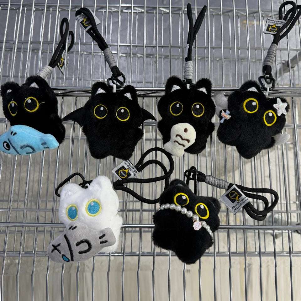 A collection of cute plush black cat keychain charms and accessories hanging on a metal grid.