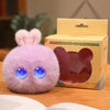 A fluffy purple rabbit plush toy with glowing blue eyes is displayed next to its packaging box.