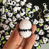 A hand holds a white and black crochet kitten keyring with a panda charm.