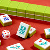 A collection of Mahjong tiles, including large colored tiles and smaller white tiles, are displayed on a red surface.