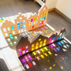 Rainbow acrylic building blocks arranged to form a house structure casting colorful light patterns on a wooden floor.