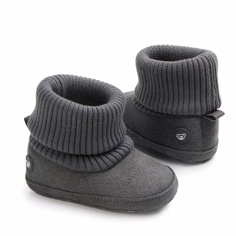 A pair of gray baby winter snow boots with ribbed cuffs and fuzzy ball accents.