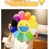 A person is holding a large, colorful sunflower plush cushion with bright petals and a smiling face.