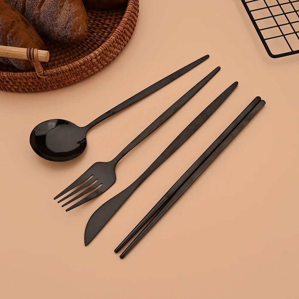 A set of six black stainless steel Korean dinnerware including a spoon, fork, and chopsticks resting on a light brown surface