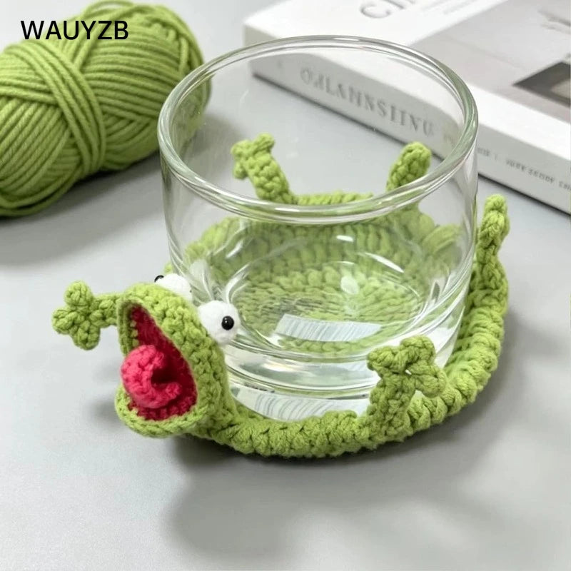 Handwoven crochet green lizard coaster with white eyes resting on a clear glass.