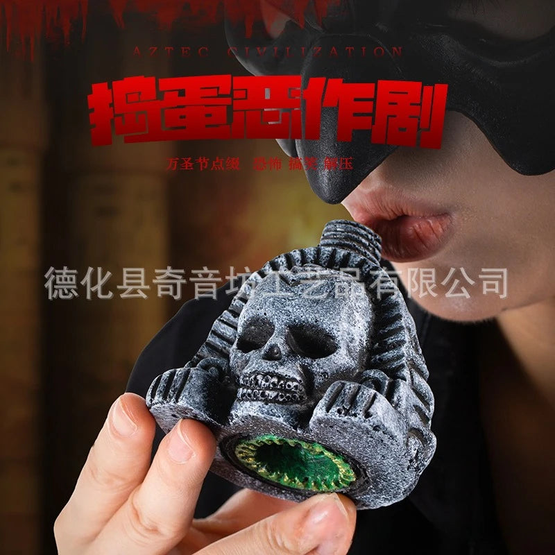 A hand holds an Aztec death whistle skull, a dark gray object with green accents, against a blurred background.