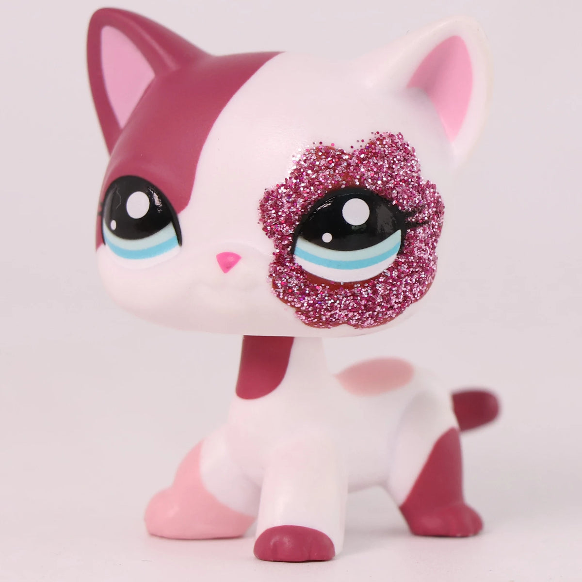 A pink and white shorthair cat bobble head figurine with glitter accents.