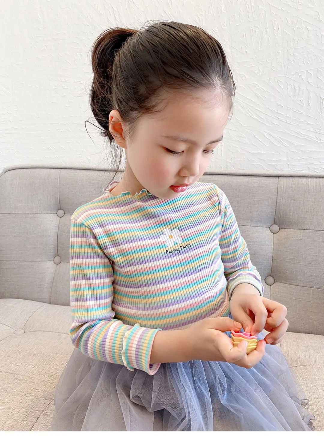 A young girl wearing a striped floral print cotton t-shirt and a tulle skirt is looking down.