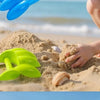 A child's hand is digging in sand with a bright green dinosaur claw toy on a beach.