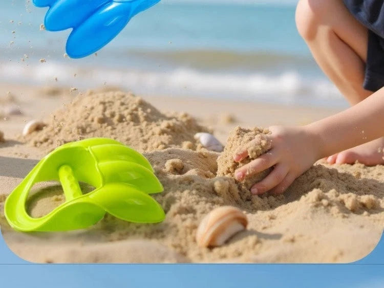 A child's hand is digging in sand with a bright green dinosaur claw toy on a beach.