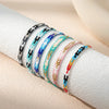 A collection of ten thin beaded bracelets in various colors and patterns laid out on a white surface.