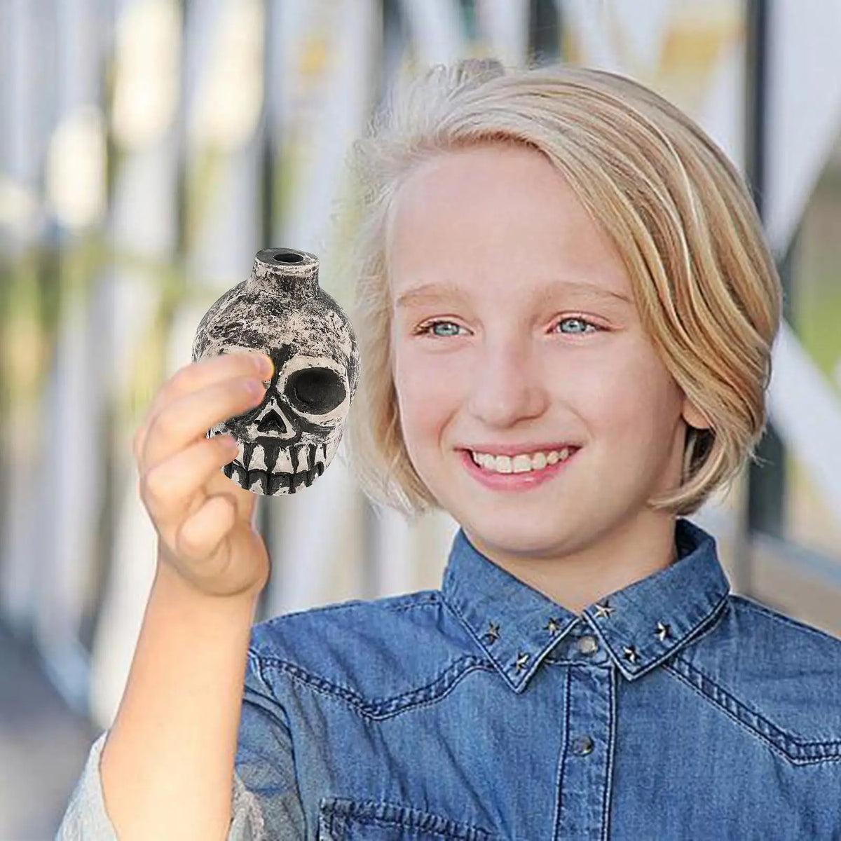 A smiling child holds up a ceramic Aztec skull whistle for the camera.