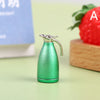 A small, metallic green miniature alloy kettle with a spout is shown on a light green surface next to a strawberry.