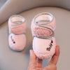 A hand holds a pair of pink plush baby snow boots with gray trim and anti-slip soles.