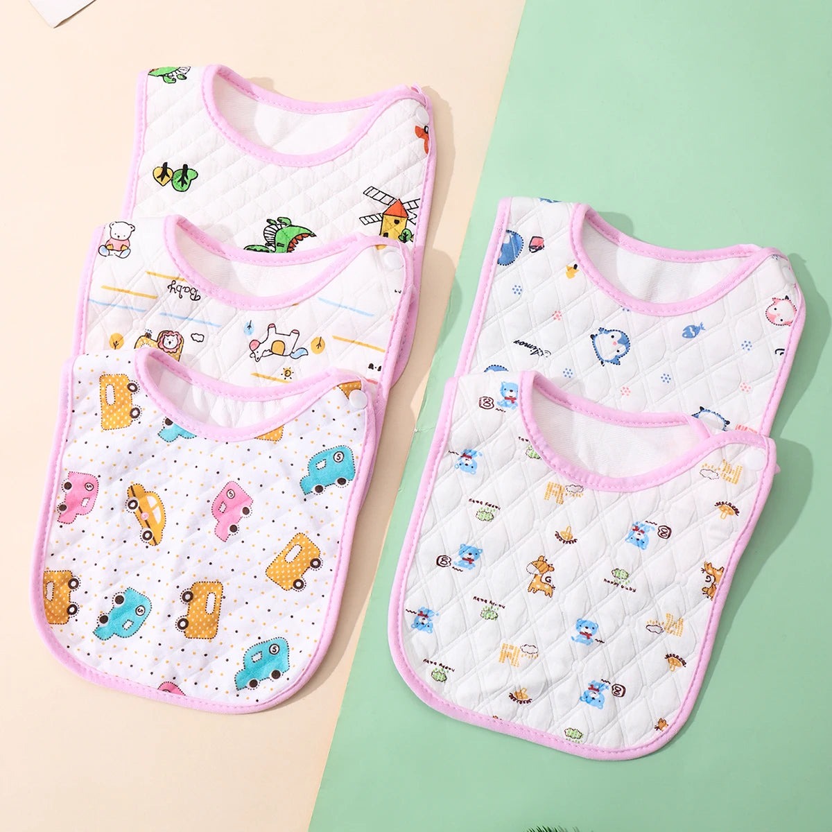 A set of three white baby bibs with colorful embroidered animals and patterns displayed on a light green background.