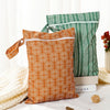 Two reusable waterproof baby wet bags in orange and green patterns resting on a white surface.