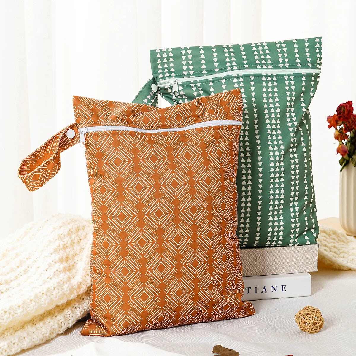 Two reusable waterproof baby wet bags in orange and green patterns resting on a white surface.