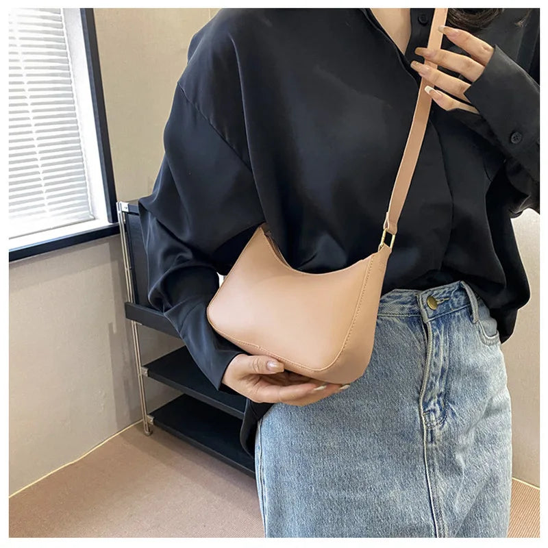 A person holds a tan PU square crossbody bag with a gold zipper closure against a dark shirt and denim jeans.