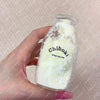 A hand holds a clear glass bottle filled with white, milky substance labeled Chiboki drink cup toy.