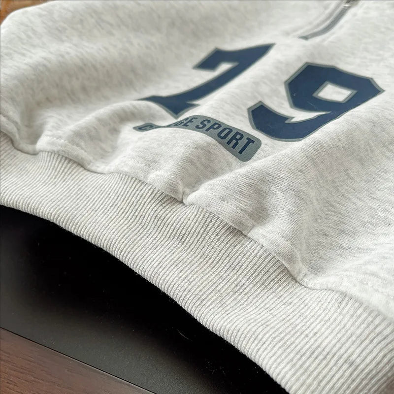 A light gray kids sweater with a large blue number 19 and the text 'THE SPORT' is shown on a dark background.