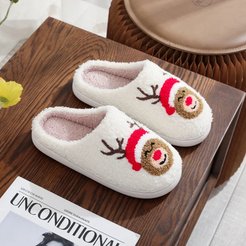 A pair of white plush indoor slippers with reindeer and Santa designs resting on a wooden tray.
