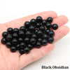 A handful of small, round black obsidian beads is held in a person's hand.