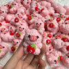 A hand holds a pile of handmade crochet mini pig keychains in various shades of pink and red.