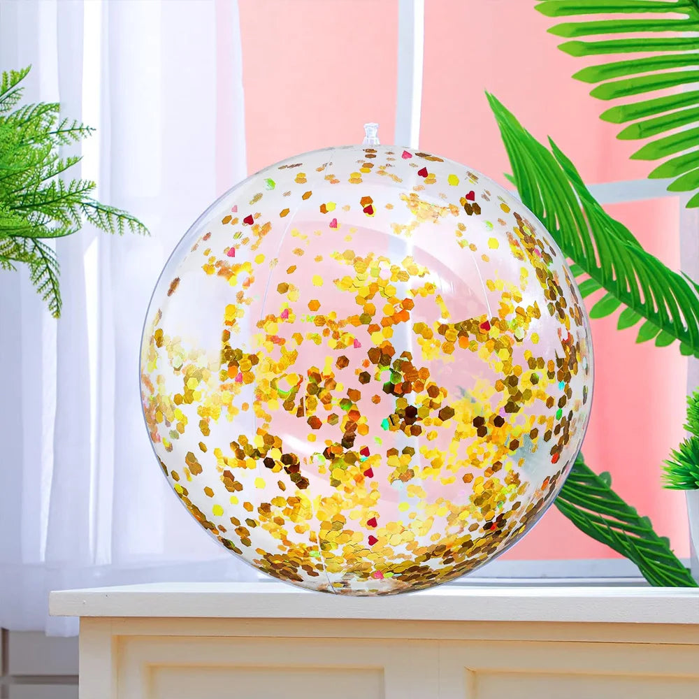 A clear inflatable beach ball filled with sparkling gold and pink sequins resting on a white surface.
