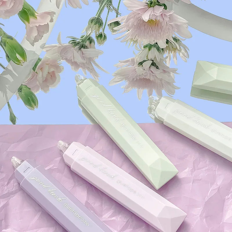 A collection of pink and green adhesive dot tape glue rollers displayed on purple and pink textured paper.