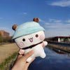 A hand holds a cute panda bear plush toy with light blue ears and a brown collar against a clear blue sky.