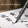 A close-up of a black pen with a soft tip writing Japanese calligraphy characters on white paper.
