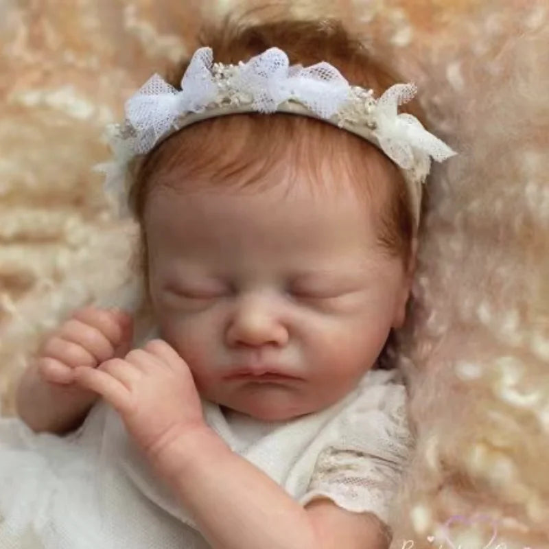A newborn baby with a white lace headband is shown, resting on a soft, light-colored fabric.