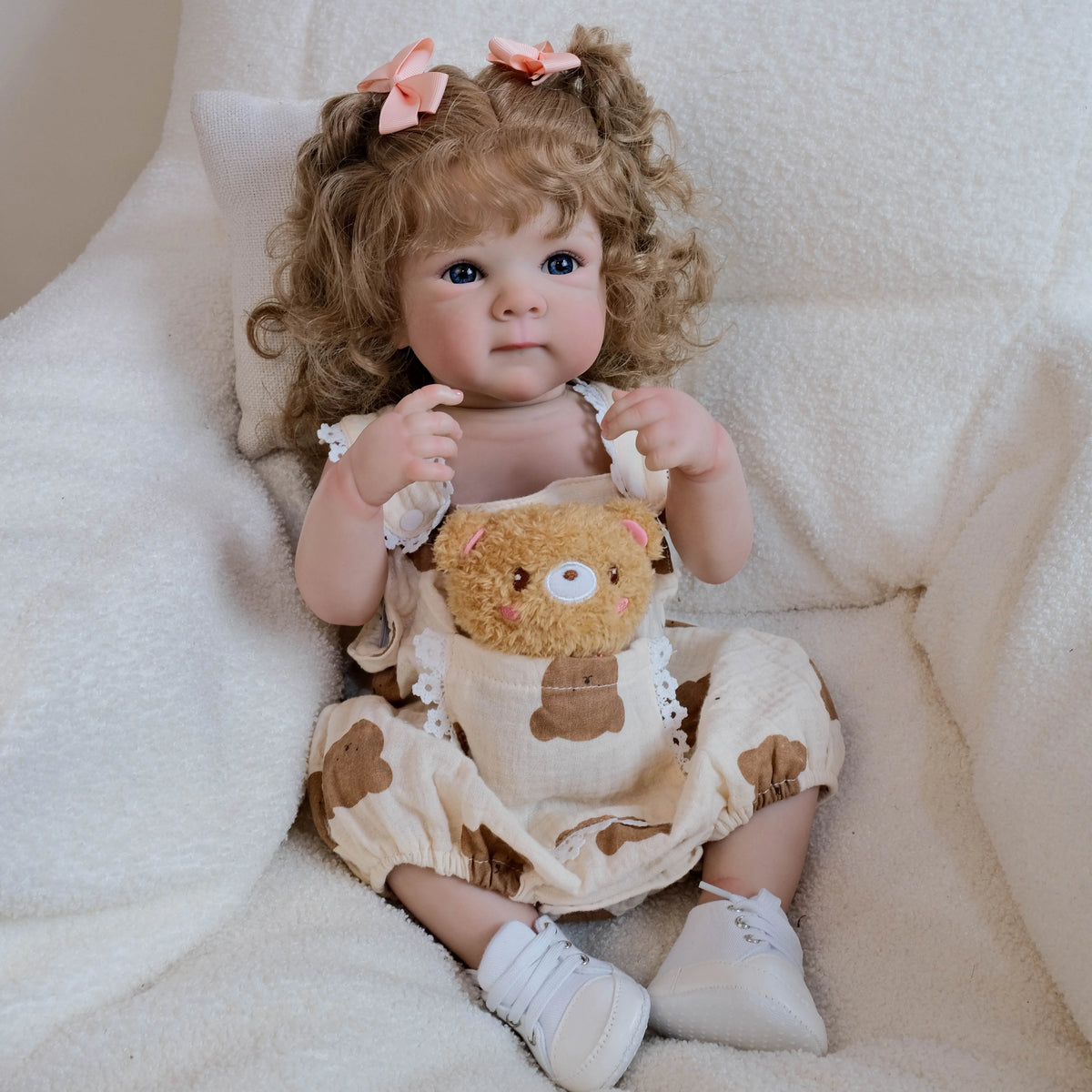 A lifelike 18-inch baby doll with hand-rooted curly hair wearing a light brown outfit and white shoes.