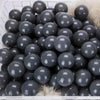 A large quantity of dark gray and black play balls are displayed in a white plastic basket.