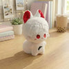 A white anime plush charm with red ears and eyes sitting on a wooden surface.