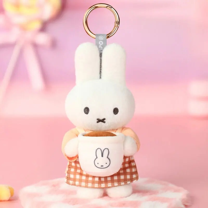 A white bunny plush keychain charm wearing a checkered apron, set against a pink background.