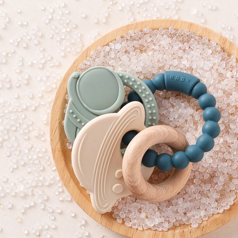 A light green silicone planet teether ring resting on a wooden board surrounded by clear crystals.
