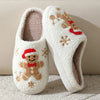 A pair of white plush indoor slippers decorated with reindeer and Christmas patterns