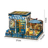 A wooden miniature dollhouse kit of a coffee shop with blue and white striped awnings and detailed interior scenes.