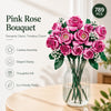 A bouquet of pink roses in a glass vase with green leaves and baby's breath flowers.