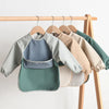 A display of various colored waterproof long-sleeved baby bibs hanging on a wooden rack.