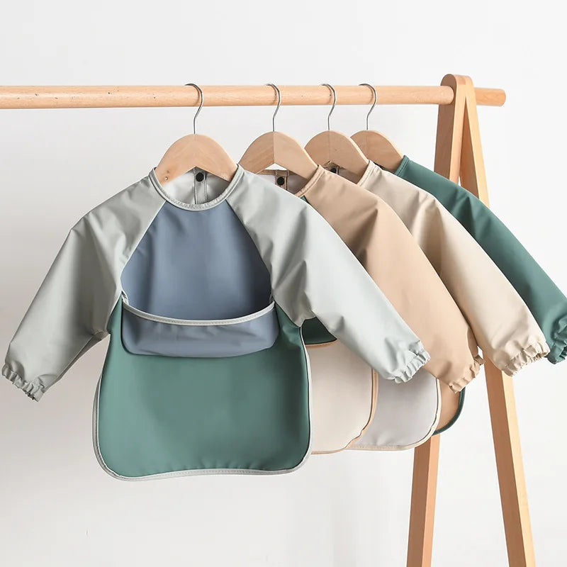 A display of various colored waterproof long-sleeved baby bibs hanging on a wooden rack.