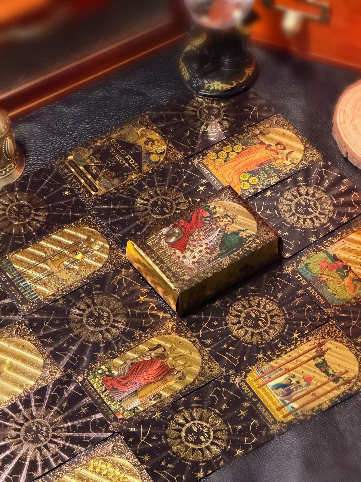 A close-up of a mini gold foil tarot card deck laid out on a dark surface with several cards visible.