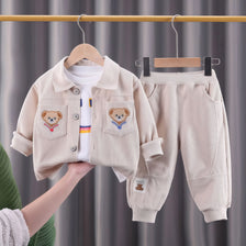 A beige corduroy tracksuit set for a child, featuring a jacket and matching pants, displayed on a hanger.