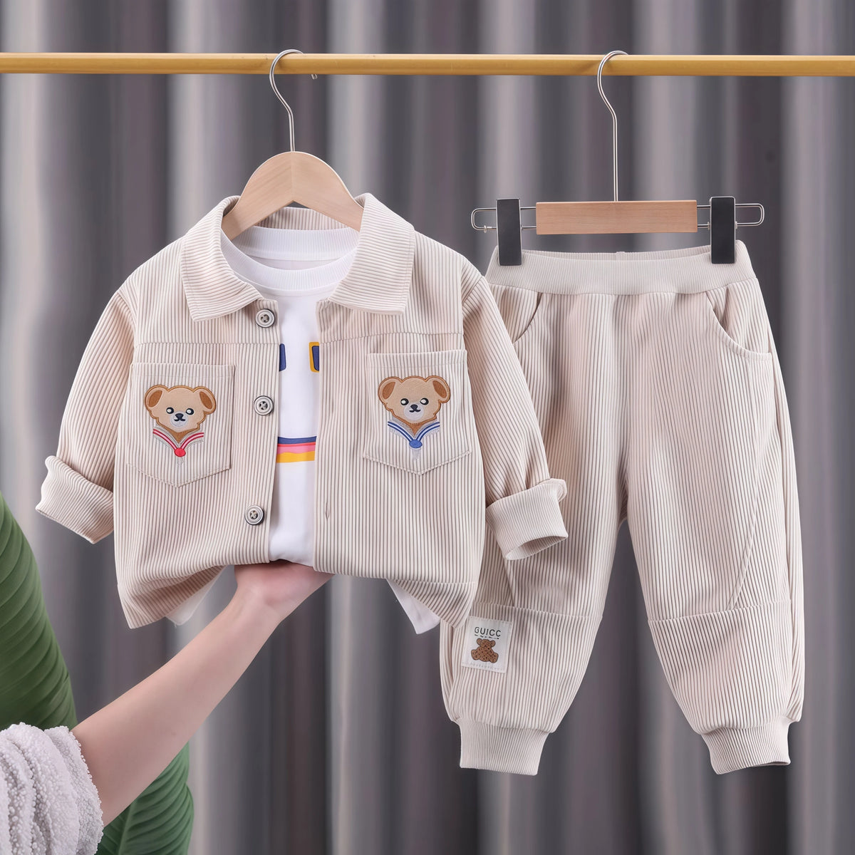A beige corduroy tracksuit set for a child, featuring a jacket and matching pants, displayed on a hanger.