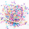 A small white bowl filled with colorful heart-shaped polymer clay sprinkles scattered on a white surface.