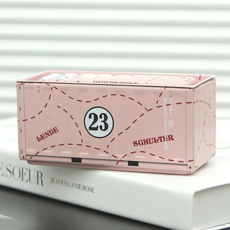 A pink miniature industrial iron storage box with an openable lid resting on a white book.