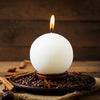 A white candle with a lit wick sits on a wooden plate surrounded by cinnamon sticks and star anise.